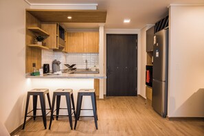 Eine moderne Küche mit Holzschränken, einem Edelstahlkühlschrank und drei Barhocker.
