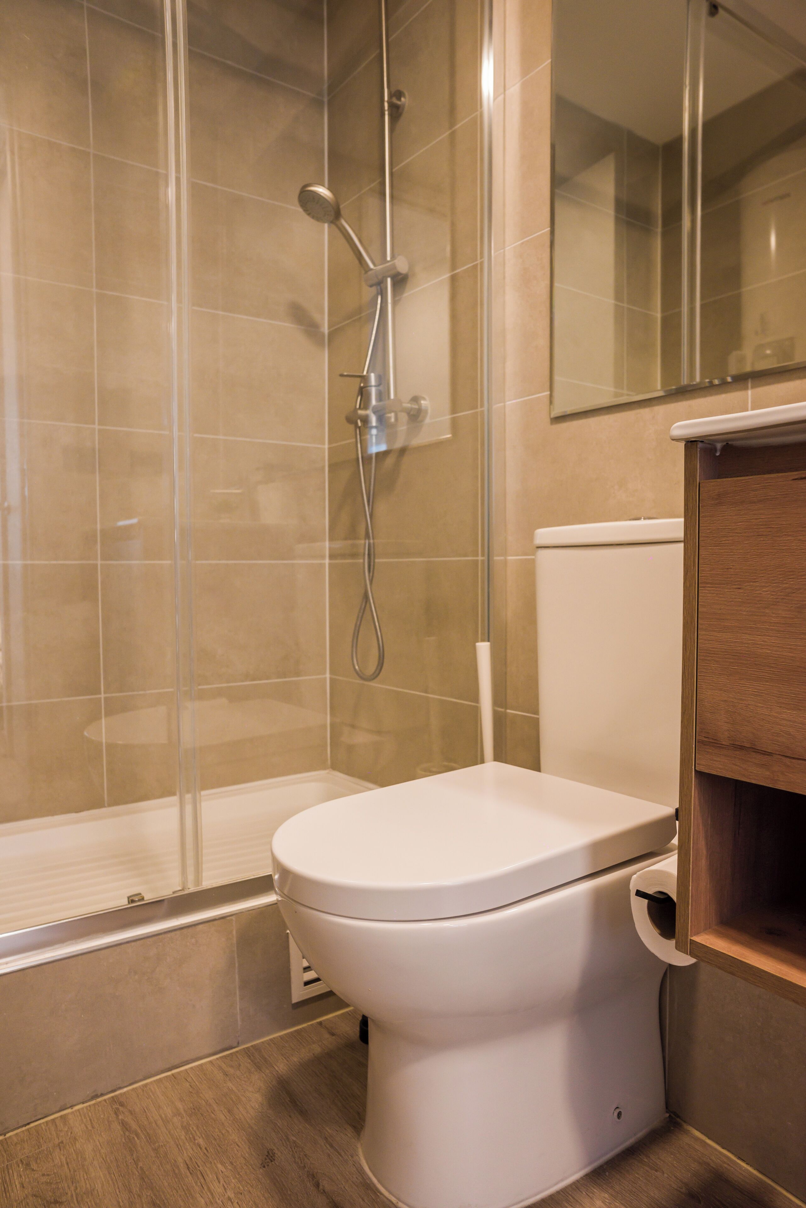 Un baño con ducha, inodoro y un armario de madera.
