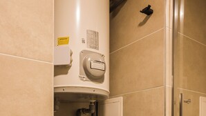 Une salle de bain avec un lave-linge noir, un chauffe-eau et une cabine de douche en verre.
