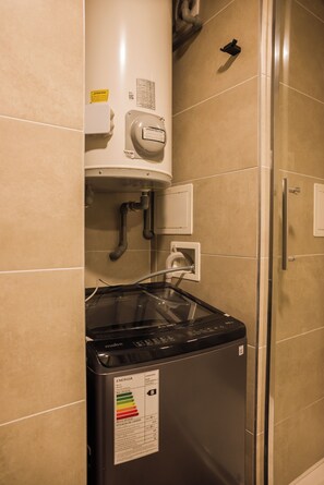 Ein Badezimmer mit einer schwarzen Waschmaschine, einem Warmwasserbereiter und einer Duschkabine aus Glas.