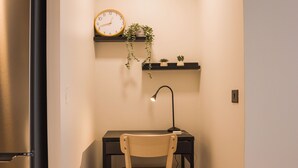 Une petite cuisine équipée d’un réfrigérateur, d’une chaise en bois, d’un bureau avec une lampe et d’une horloge murale.