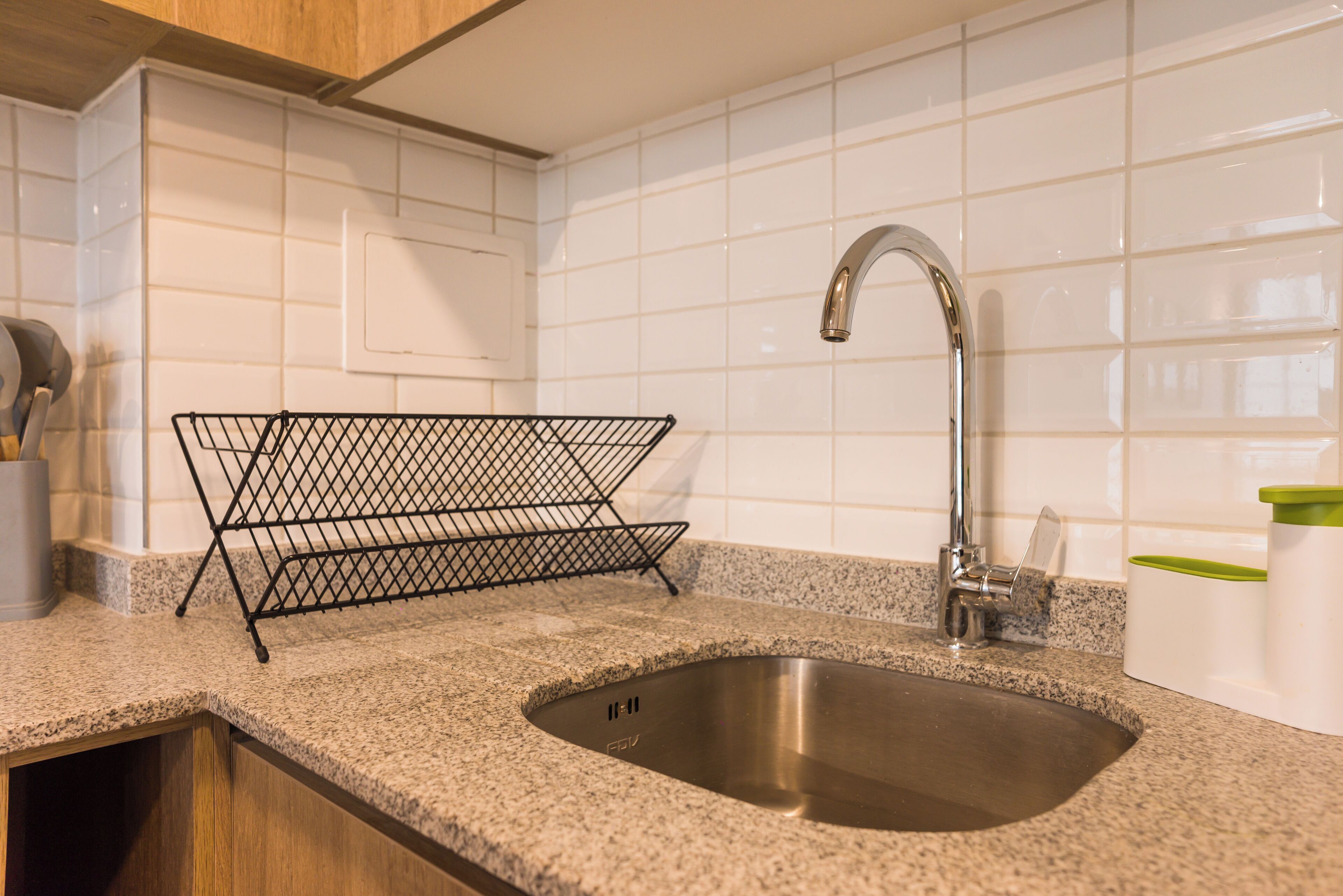 Una cocina con un lavamanos de acero inoxidable, un escurreplatos de alambre y una encimera de granito.