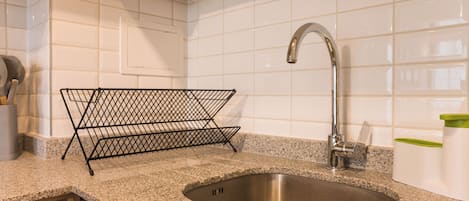 A kitchen with a stainless steel sink, a wire rack, and a granite countertop.