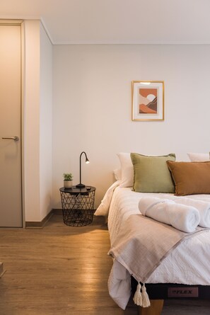 Ein Schlafzimmer mit einem Bett, einem Nachttisch mit Lampe, einer kleinen Topfpflanze und einem gerahmten Bild an der Wand.