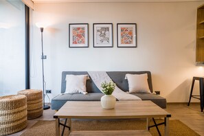 Un salon moderne avec un canapé gris, une table basse en bois et trois œuvres d’art florales encadrées accrochées au mur.