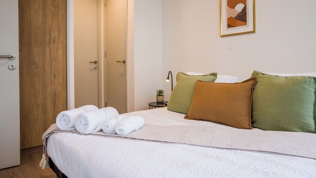 Une chambre d’hôtel avec un lit, une porte, une petite table avec une plante et un tableau accroché au mur.
