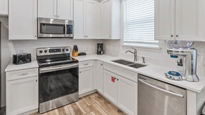 A modern kitchen with white cabinetry, stainless steel appliances, a built-in oven, a microwave, a coffee maker, and a dishwasher. - Cozy 2-bedroom house 10 minutes to Disney! (Kissimmee)