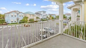 A covered balcony with a view of a row of pastel-colored townhouses, a parking area, and a small garden. - Cozy 2-bedroom house 10 minutes to Disney! (Kissimmee)