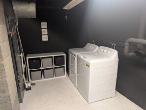 Ein Waschraum mit zwei Waschmaschinen mit Frontlader, einer Sitzbank mit Aufbewahrungsboxen und einem an der Wand befestigten Schild, das Waschen, Trocknen und Falten anzeigt.