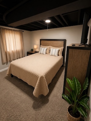 A bedroom with a large bed, bedside tables, a desk with a computer, and a potted plant.