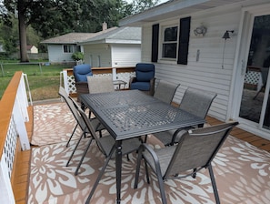 Eine überdachte Terrasse mit einem Metalltisch und -stühlen, ein Holzboden und ein Blick auf ein Haus im Hintergrund.
