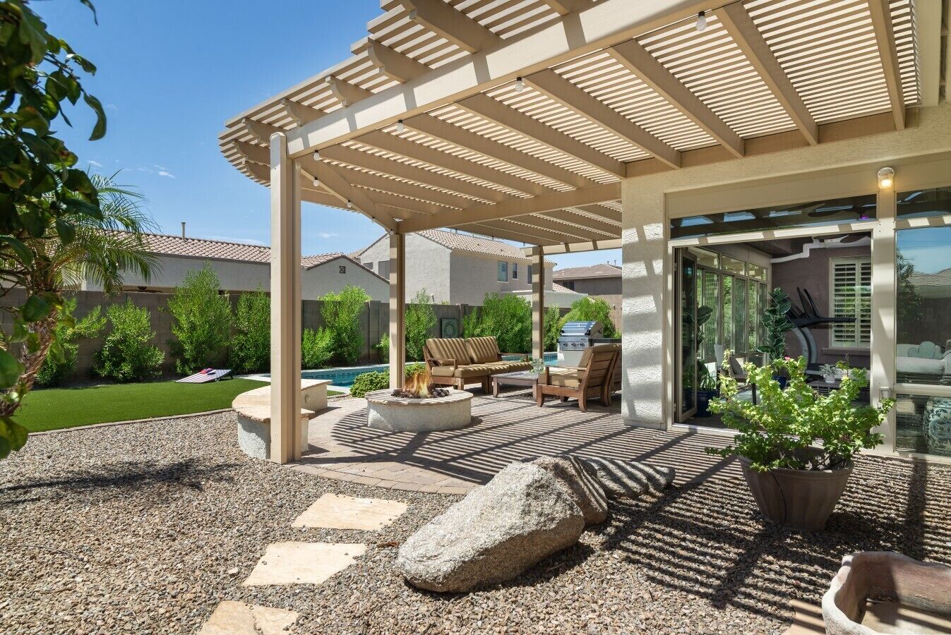 Un patio cubierto con mobiliario exterior, una parrilla y una piscina al fondo.