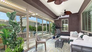 A spacious indoor area with a large window, a ceiling fan, and a seating area with a sofa and a chair. - Luxury Retreat | Heated Pool•Game Room•Fire Pit (Gilbert)