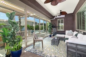 Ein großzügiger Innenbereich mit großem Fenster, Deckenventilator und einer Sitzecke mit Sofa und Sessel.
