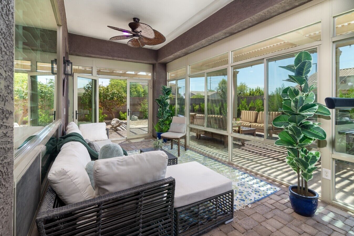 A sunroom with a ceiling fan, large windows, and outdoor seating.