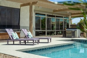 Ein moderner Poolbereich im Freien mit Liegestühlen und einer Pergola.
