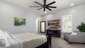 A bedroom with a bed, a fireplace, a television, and a ceiling fan. - Luxury Retreat | Heated Pool•Game Room•Fire Pit (Gilbert)