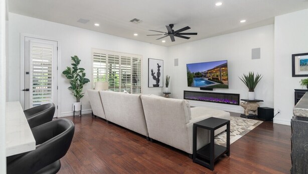 A modern living room with a sofa, TV, ceiling fan, and a fireplace. - Luxury Retreat | Heated Pool•Game Room•Fire Pit (Gilbert)