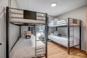 Ein Zimmer mit zwei Etagenbetten, einem Fenster mit Vorhängen, einem Nachttisch mit Lampe und einem Kuscheltier auf einem Bett.