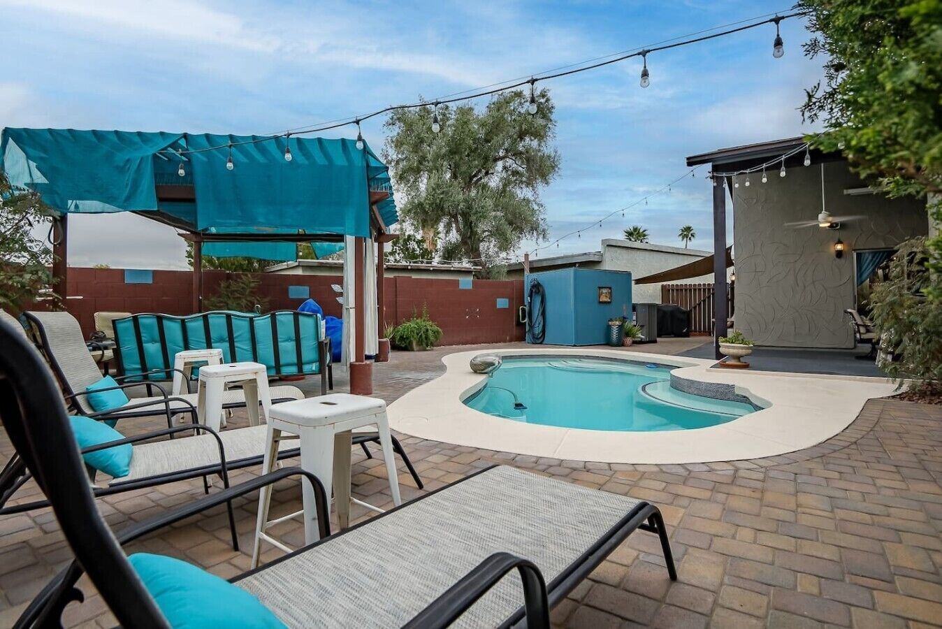 A backyard with a swimming pool, lounge chairs, and a covered patio area.
