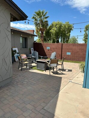 Eine Terrasse mit Gartenmöbeln, einem Feuerkorb und Lichterketten.