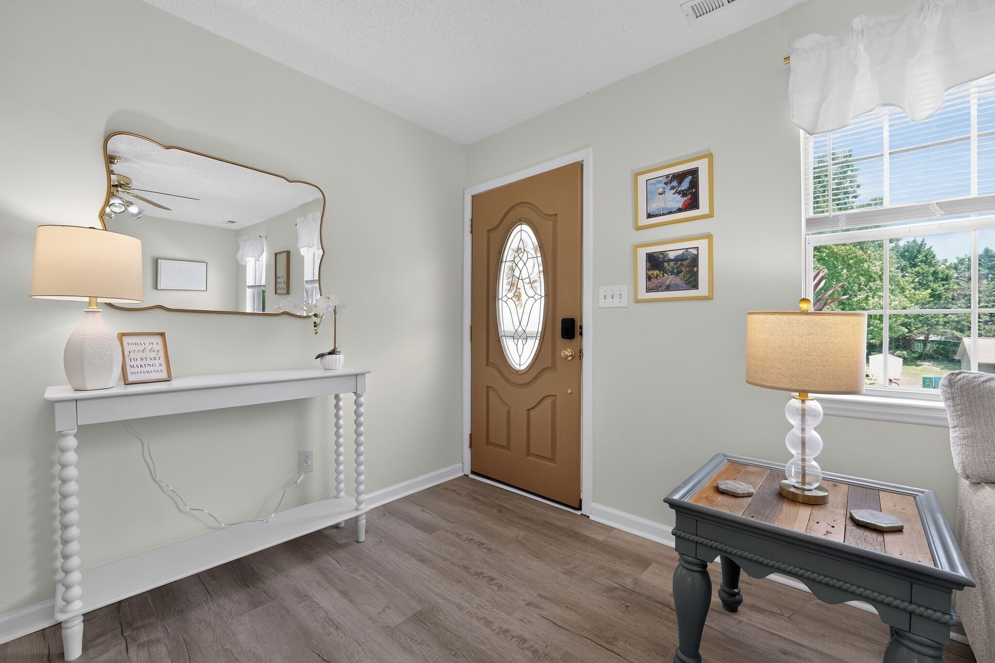 A hallway with a wooden door, a console table with a lamp, and framed pictures on the wall.