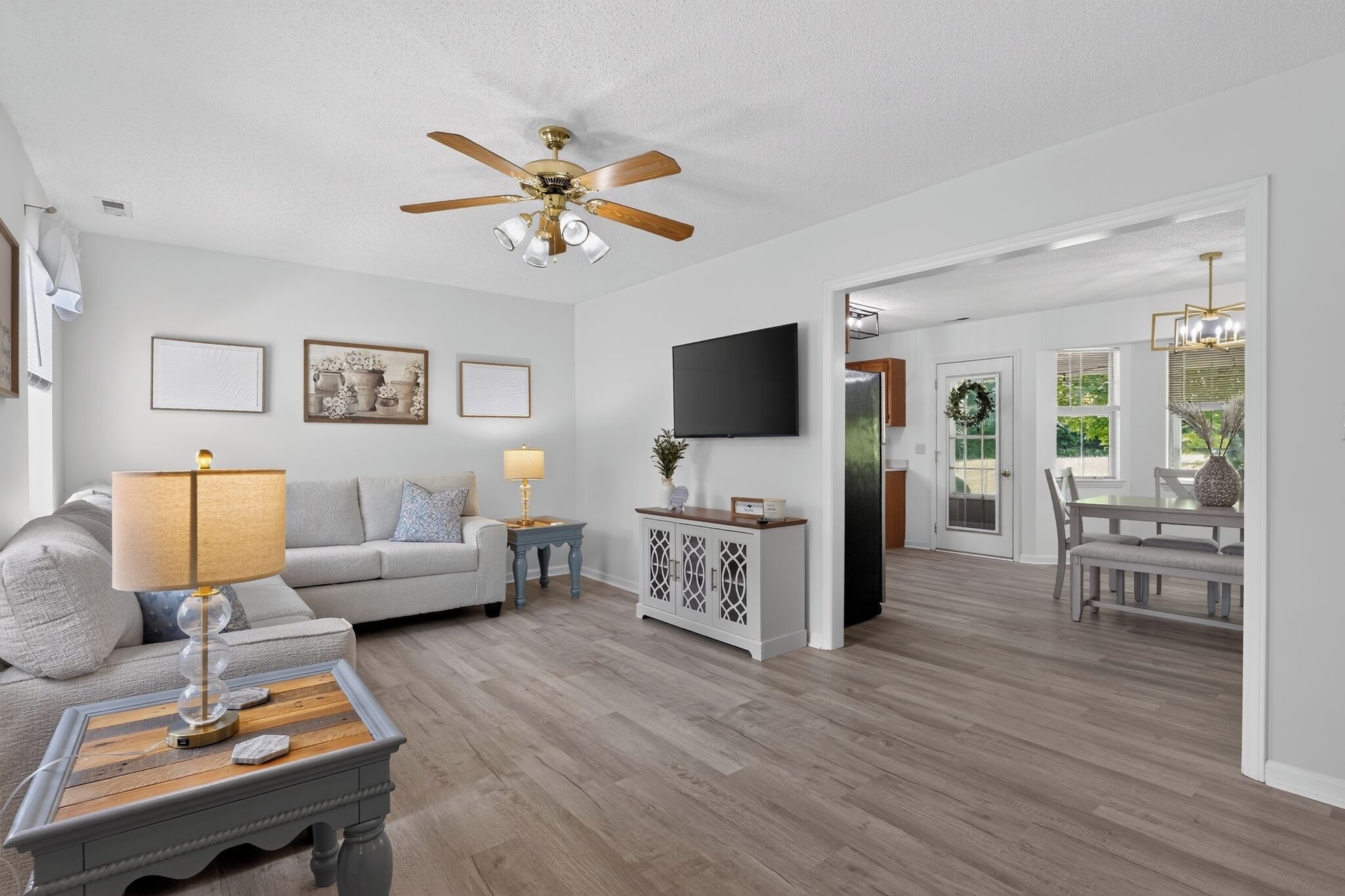 A modern living room with a ceiling fan, a flat-screen TV, and a dining area with a chandelier.