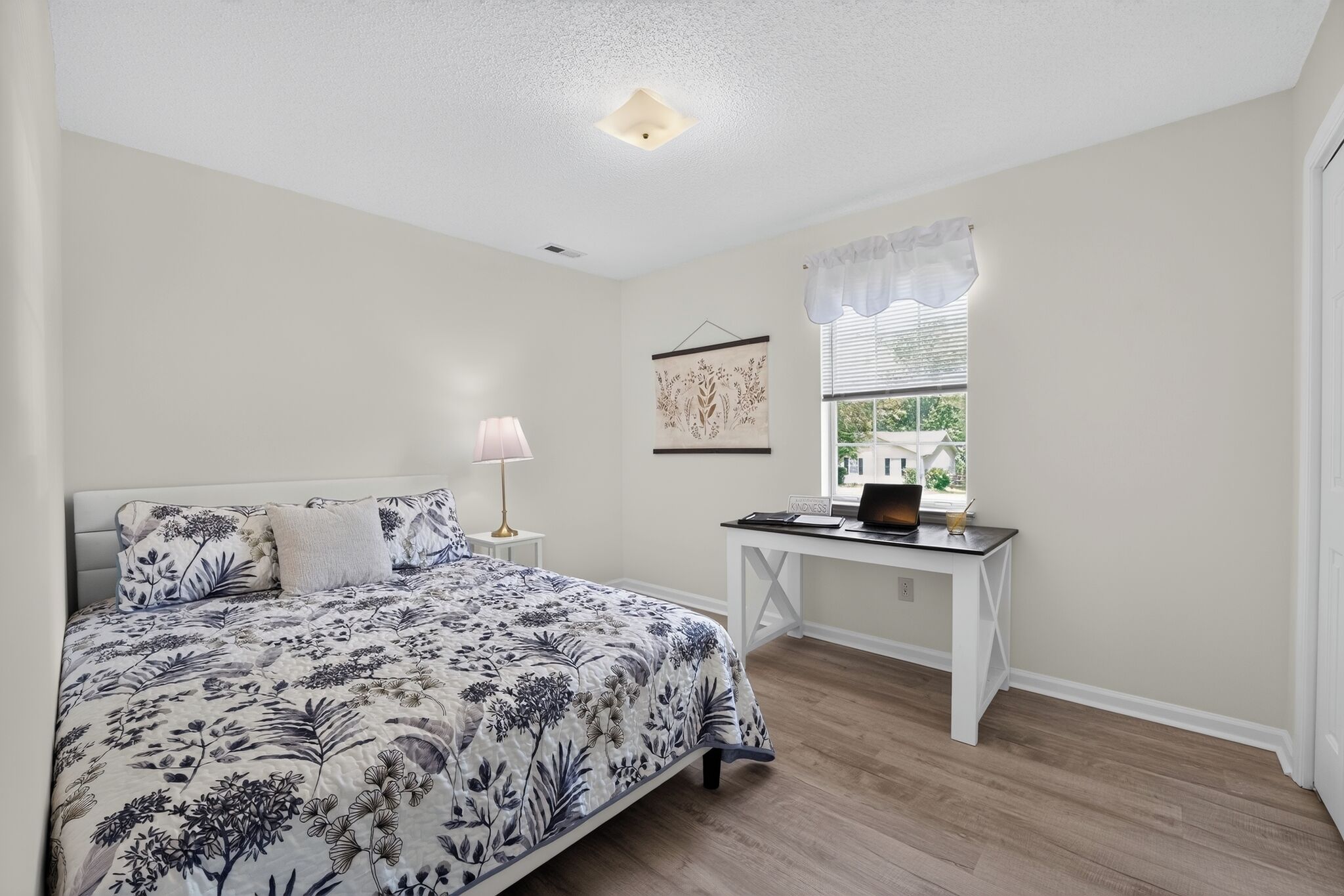A bedroom with a bed, a desk, a lamp, and a window with blinds.