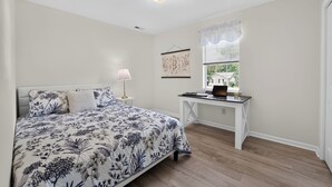 A bedroom with a bed, a desk, a lamp, and a window with blinds.
