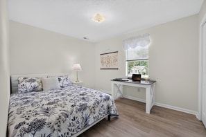 A bedroom with a bed, a desk, a lamp, and a window with blinds.