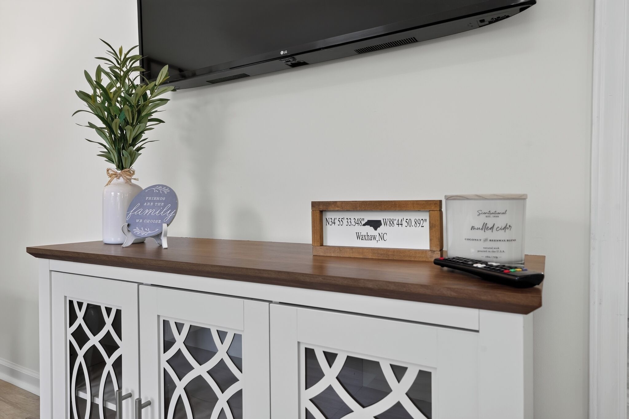 Un salon moderne avec un téléviseur à écran plat fixé au mur, une table basse en bois et un panneau décoratif indiquant des coordonnées géographiques.