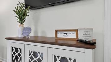 Un salon moderne avec un téléviseur à écran plat fixé au mur, une table basse en bois et un panneau décoratif indiquant des coordonnées géographiques.
