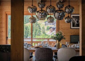 Un espace repas avec un décor intérieur en bois, une table dressée pour le repas et une vue sur un paysage montagneux, visible à travers de grandes fenêtres.