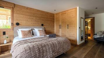 Un dormitorio con cabecera de madera, cama con manta suave, mesita de noche con un florero y armario con espejo.