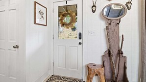 A white door with a glass panel, a framed picture, a wooden stool, and a mirror with a skull decoration. - Long & Short of It - Pet Friendly, EV Charger, Firepit + Big Canoe Access (Jasper)