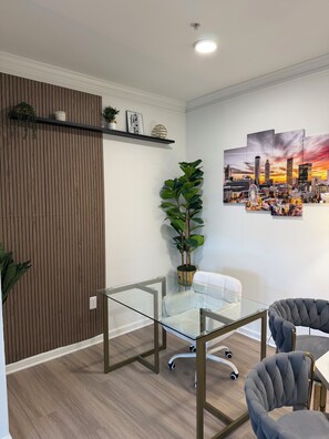 A modern office space with a glass table, two chairs, a potted plant, and a cityscape painting on the wall. - Elegant Atlanta Suite-FREE Parking, Ideal For Long Stays! (Atlanta)