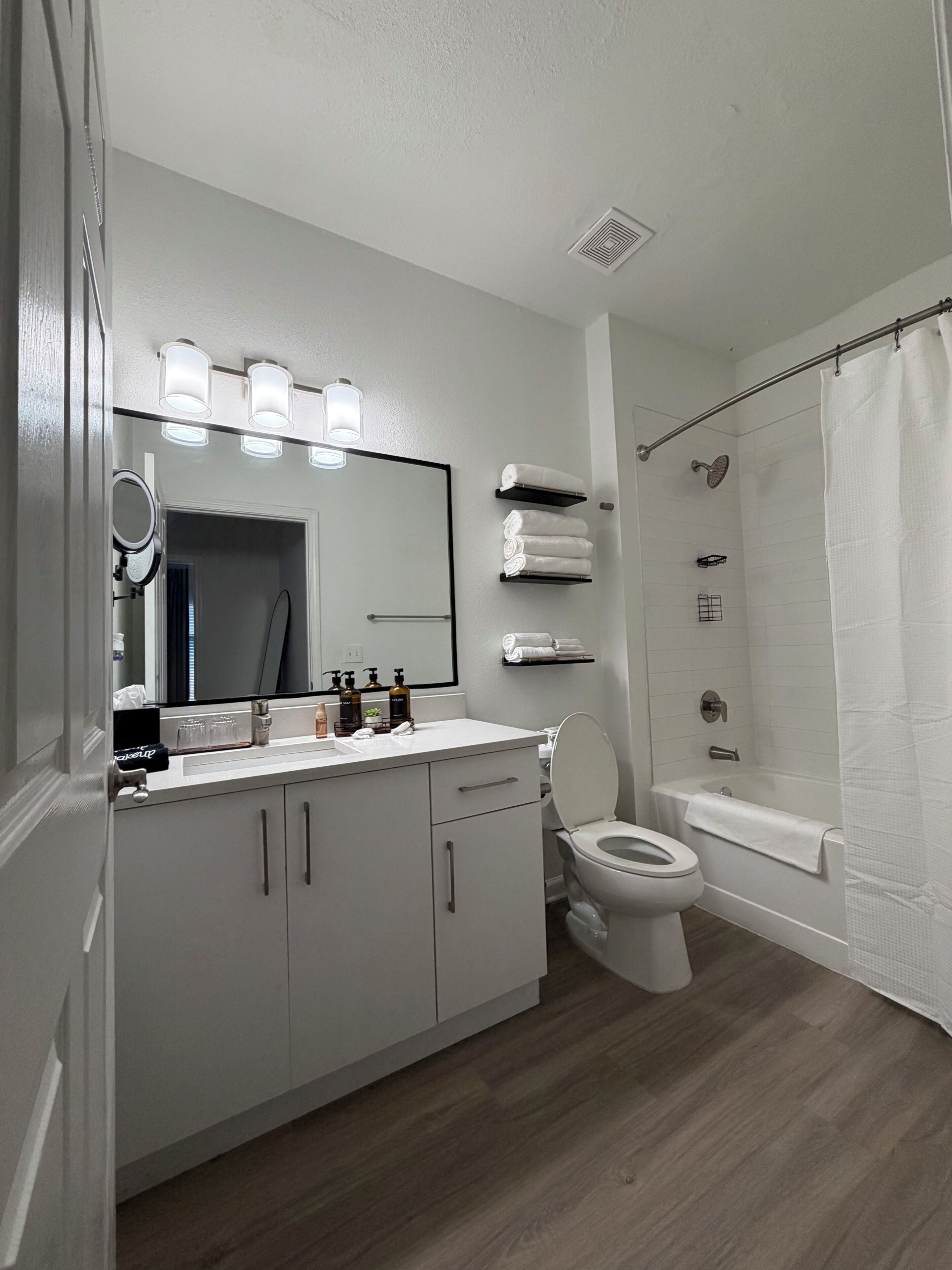 A modern bathroom with a white vanity, a toilet, a bathtub, and a shower curtain.