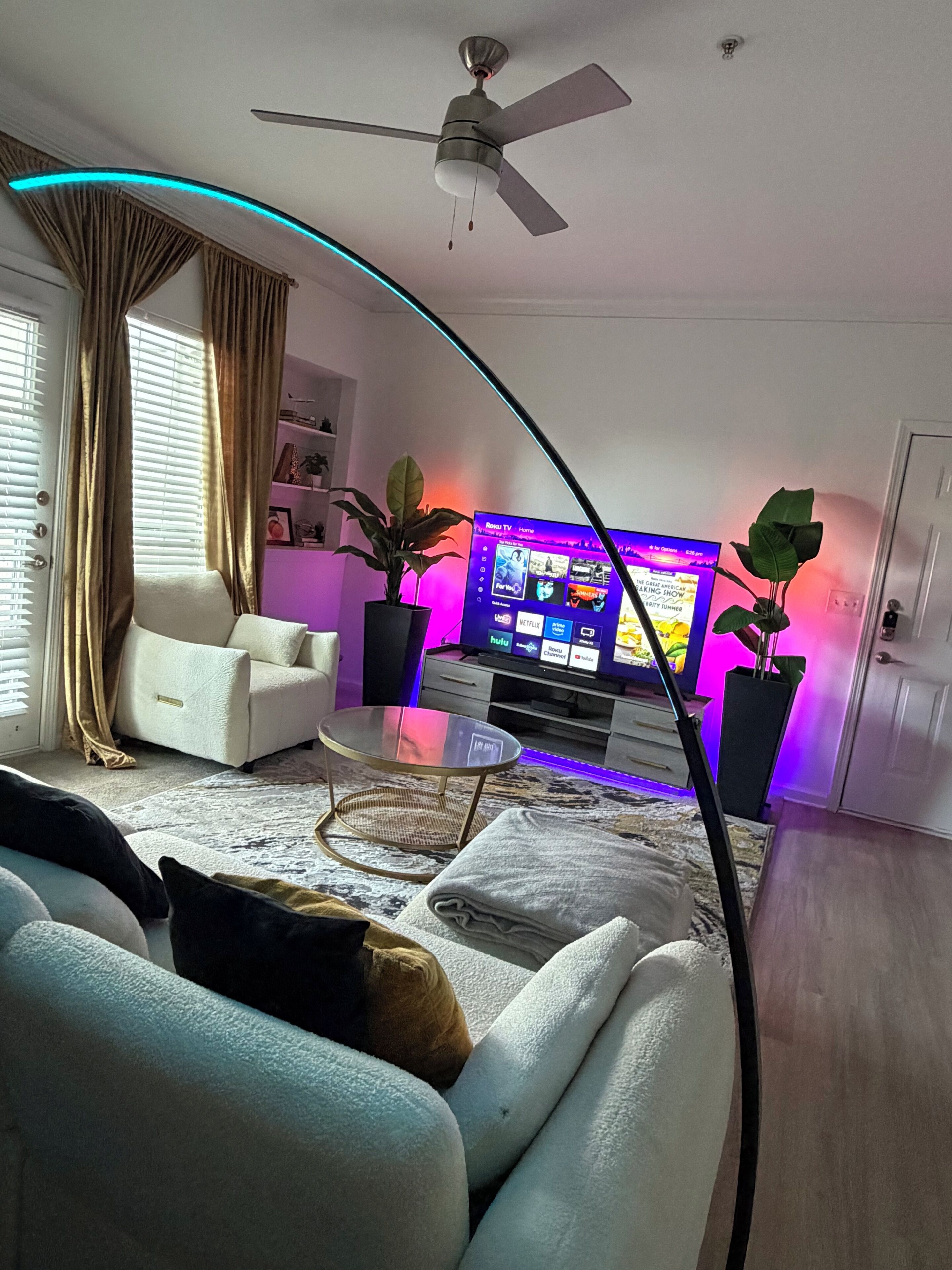 A modern living room with a flat-screen TV, a ceiling fan, and a glass coffee table.
