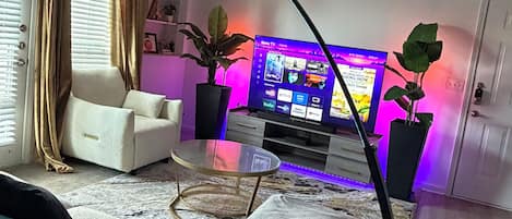 A modern living room with a flat-screen TV, a ceiling fan, and a glass coffee table.
