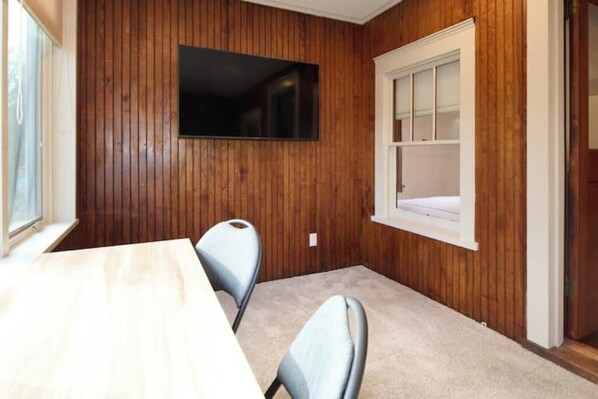 Una habitación con pared de paneles de madera, un televisor de pantalla plana sobre una ventana y piso alfombrado.