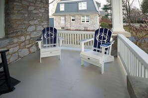 A porch with two Adirondack chairs, a stone wall, and a house in the background.