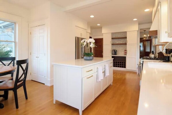 A modern kitchen with white cabinetry, a central island, and a dining area with a wooden table and chairs.