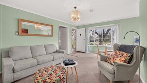 Una sala con un sofá gris, un otoman estampado, una mesita redonda pequeña y un sillón gris con un cojín colorido.