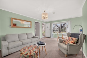 A living room with a grey sofa, a patterned ottoman, a small round table, and a grey armchair with a colorful cushion. - Grace Cottage - Peaceful Vineyard Escape in the Barossa Valley (Penrice)