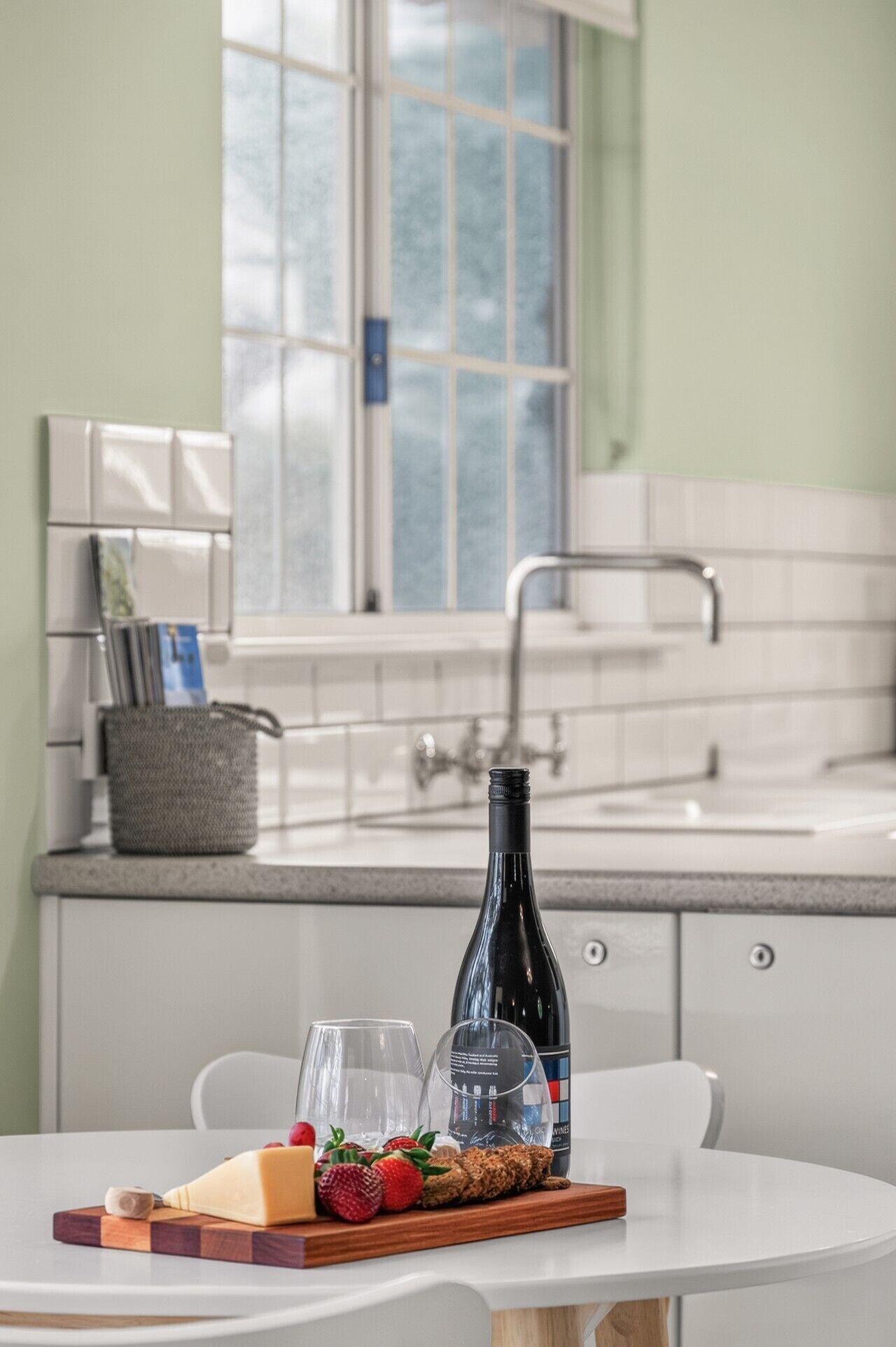 A kitchen with a dining table set with food and wine, a window, and a sink.