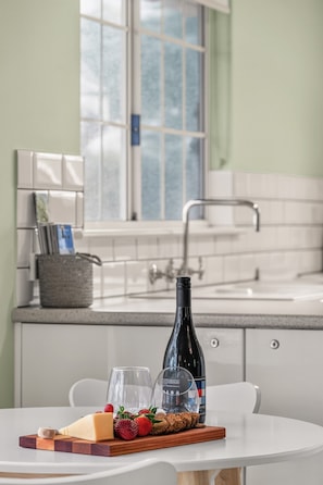 A kitchen with a dining table set with food and wine, a window, and a sink. - Grace Cottage - Peaceful Vineyard Escape in the Barossa Valley (Penrice)