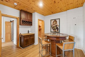 A wooden-paneled room with a round table and chairs, a wine rack, and a framed picture on the wall. - Painted Sky Cabin - Long Distance Mountain Views! | Firepit | Pet Friendly (Morganton)