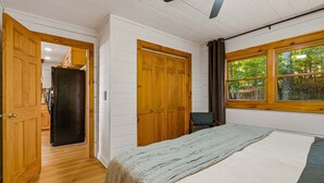 Ein Schlafzimmer mit einem Bett, einem Holzschrank und einem Fenster mit Blick auf Bäume.