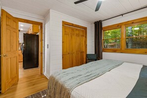 Ein Schlafzimmer mit einem Bett, einem Holzschrank und einem Fenster mit Blick auf Bäume.