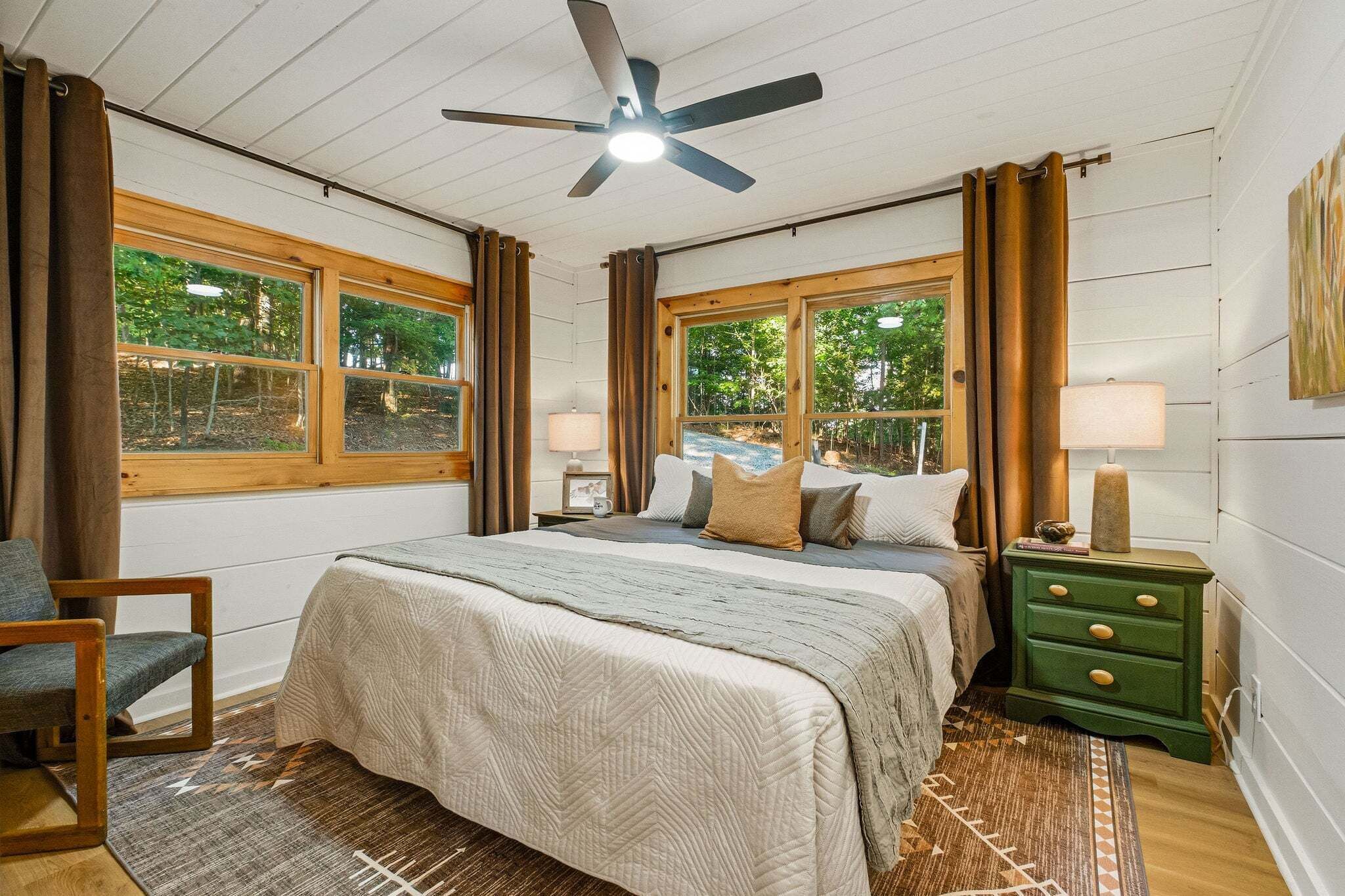 A bedroom with a bed, a chair, a nightstand, a lamp, and a ceiling fan.